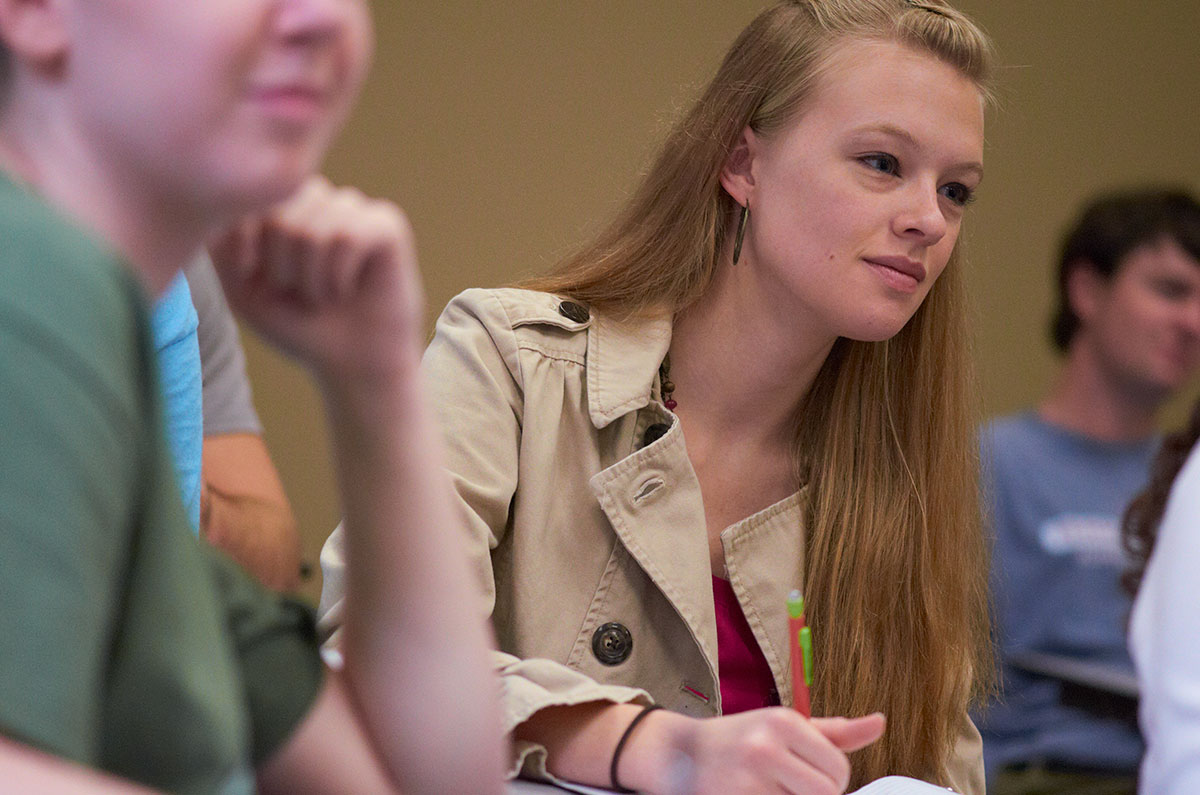 Female student leans over a desk listening to a lecture