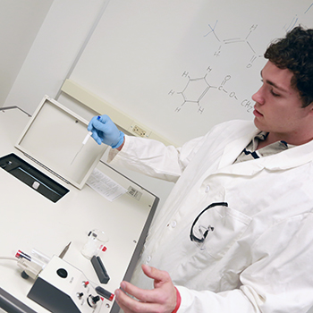 Student in lab coat inserting a sample into the NMR machine in Hudson Lab Sciences Building